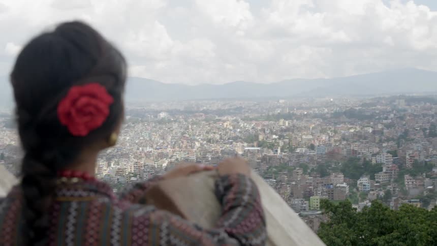 A woman with a rose in her hair overlooks the city below her