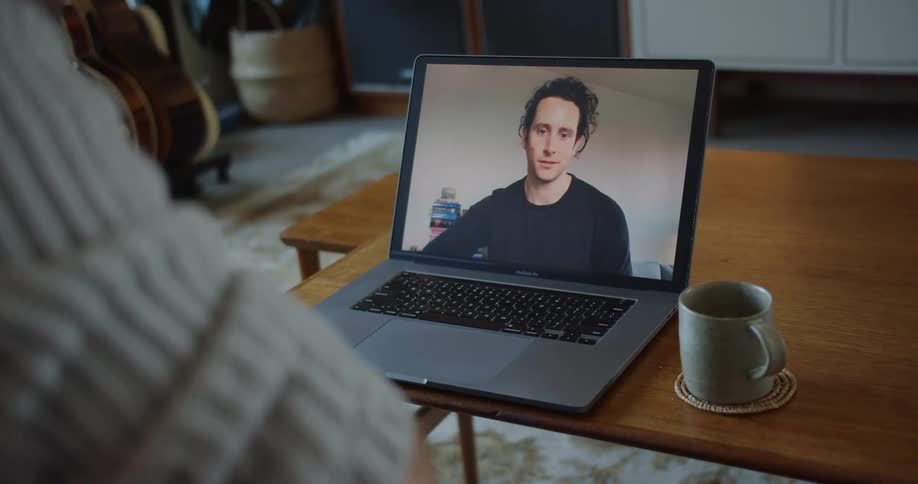 A man sits on his couch during a video call with another man on his laptop