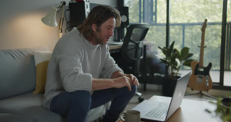 Man sitting in a couch at home talking on a video call on a laptop