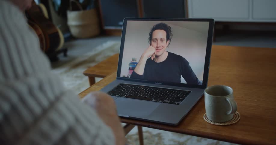 A man gestures with his hands as he talks to another during a video call on his laptop