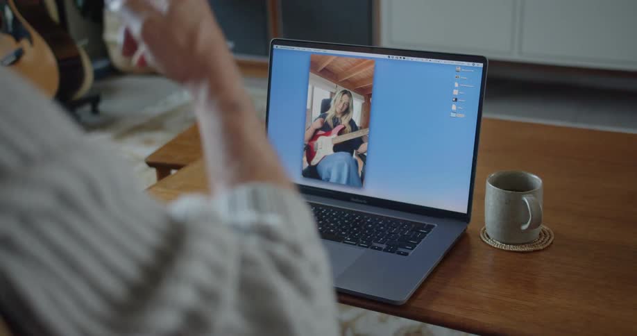 A man moves his fingers to the beat as he watches a woman he is video chatting with play the guitar and sing