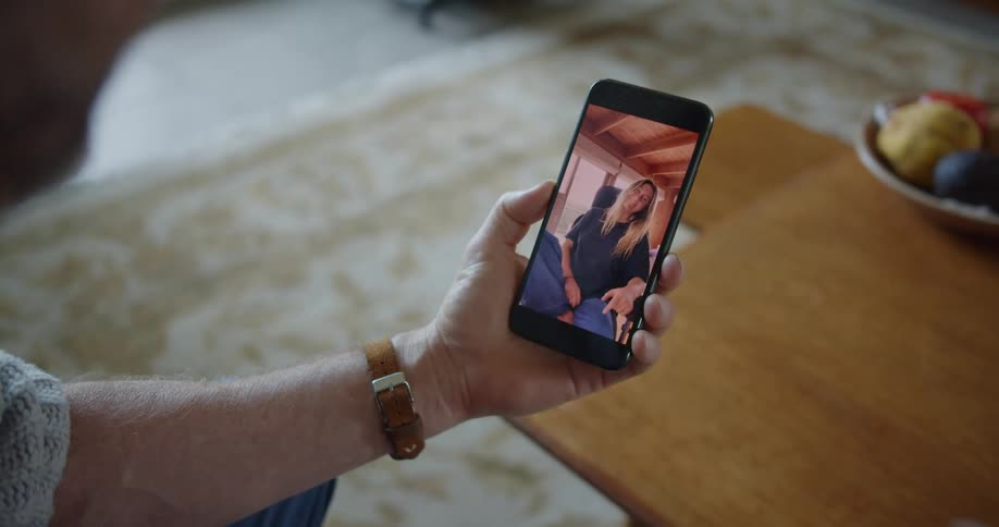 A man uses video chat on a smartphone to wave at a woman who returns the gesture
