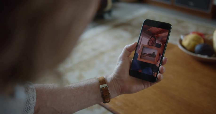A woman showing framed pictures on a video call on the phone with a man at home