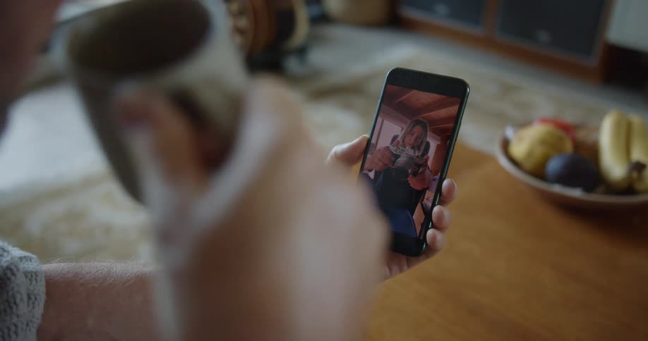 Man drinks a cup of coffee and makes a video call with blonde woman holding a camera on his smartphone