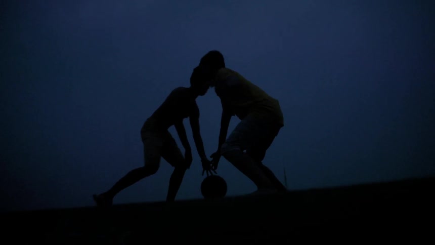 Two people are playing basketball in a dark area