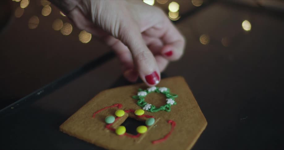 A woman places a snowflake shaped sprinkle on wreath shaped frosting on a gingerbread house