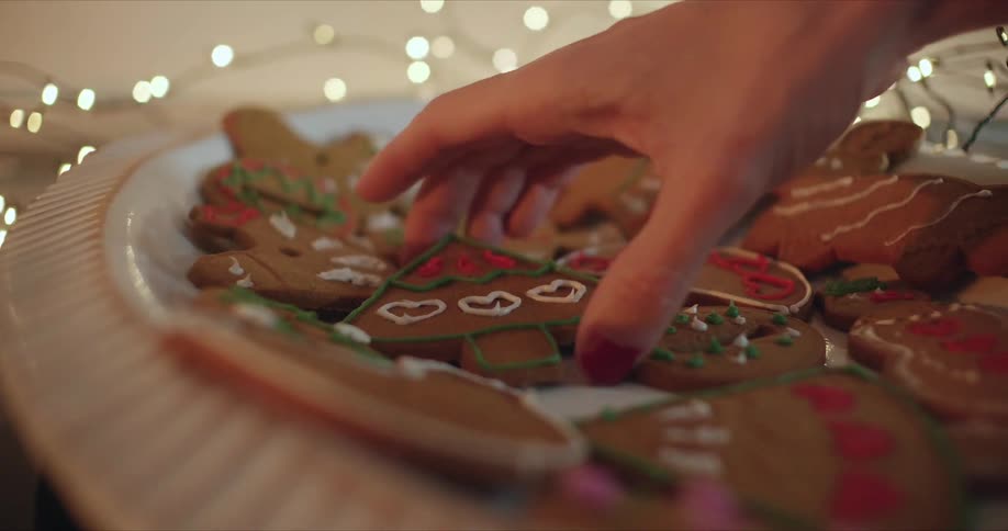 A woman retrieves a gingerbread cookie in the shape of a christmas tree from a plate
