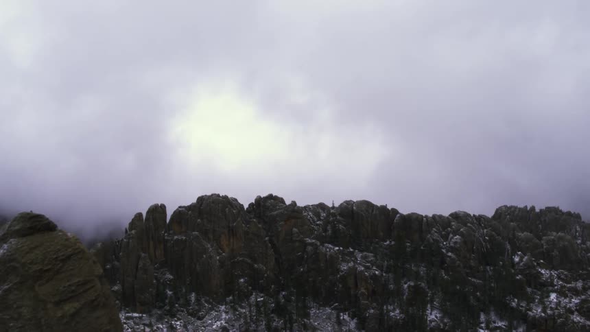 White cloud floats over snow covered rough mountain terrain in overcast sky