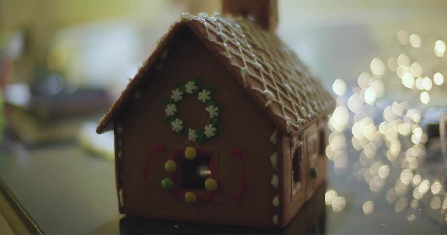 A beautifully decorated gingerbread house sits on a table in front of fairy lights