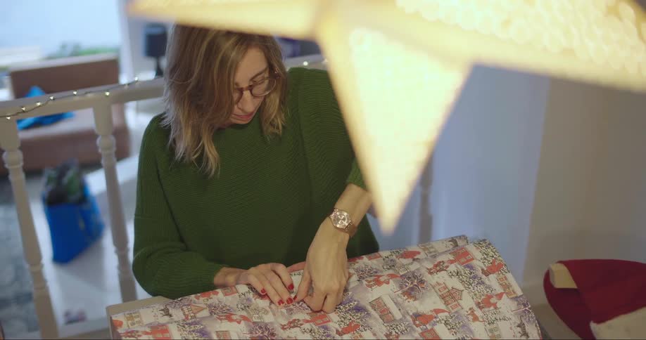 Woman is wrapping a gift and another person hands her some tape