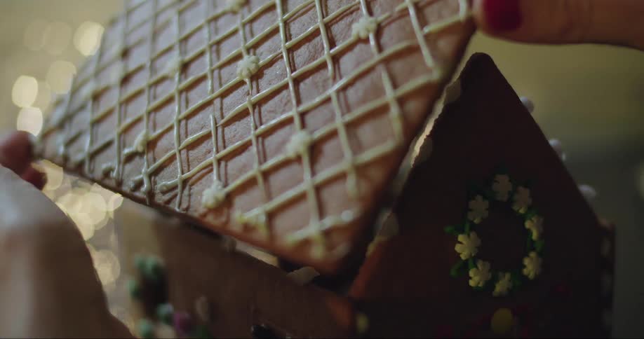 A baker assembles a gingerbread house roof onto a beautifully decorated gingerbread house