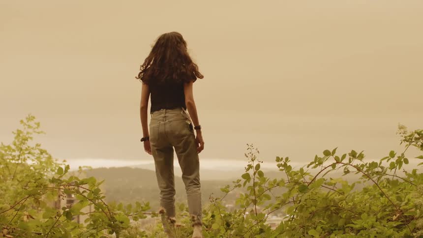 A woman runs to the edge of a hill and overlooks the smoky landscape