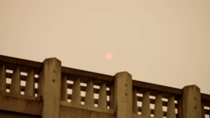 The stone railing of a bridge under a cloudy orange evening sky