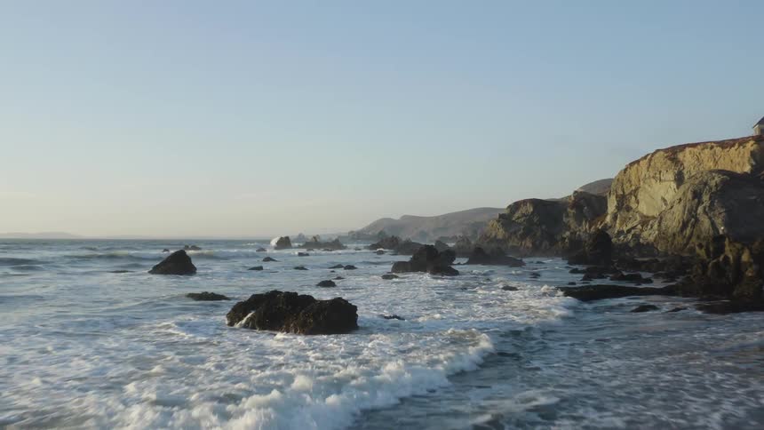 Aerial view of a coast where tide meets land next to a sea side cliff