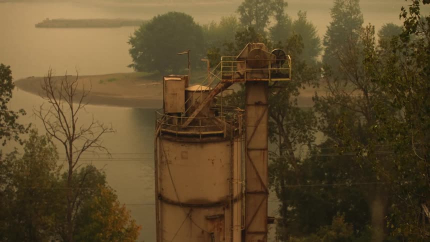 A steel upright structure surrounded by trees and a body of water on a hazy day
