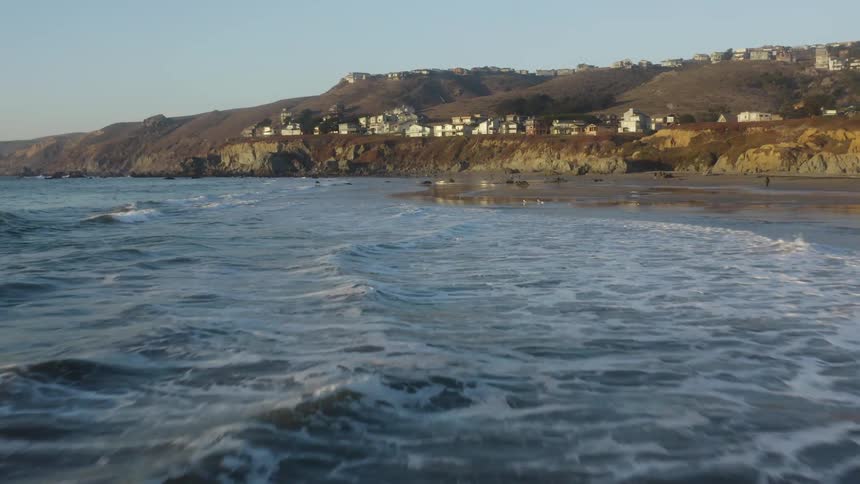 Ocean waves wash into a beach below a town on a clear day