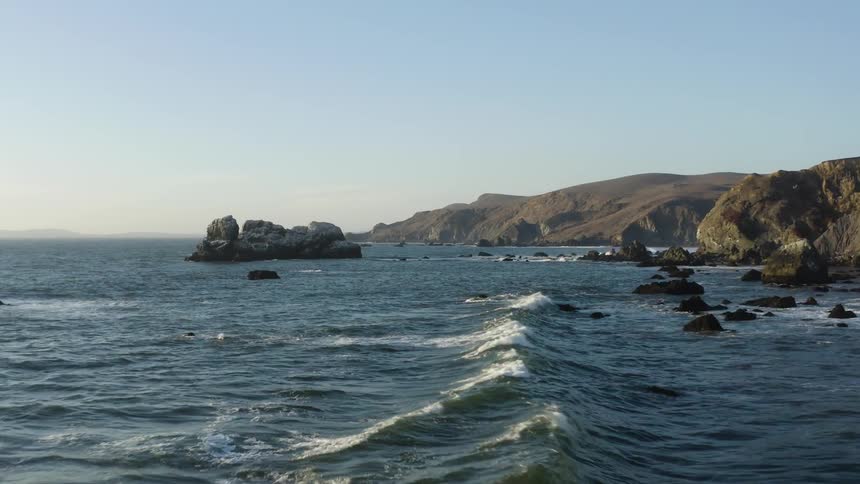 Small waves crash on boulders in the ocean near a cliff