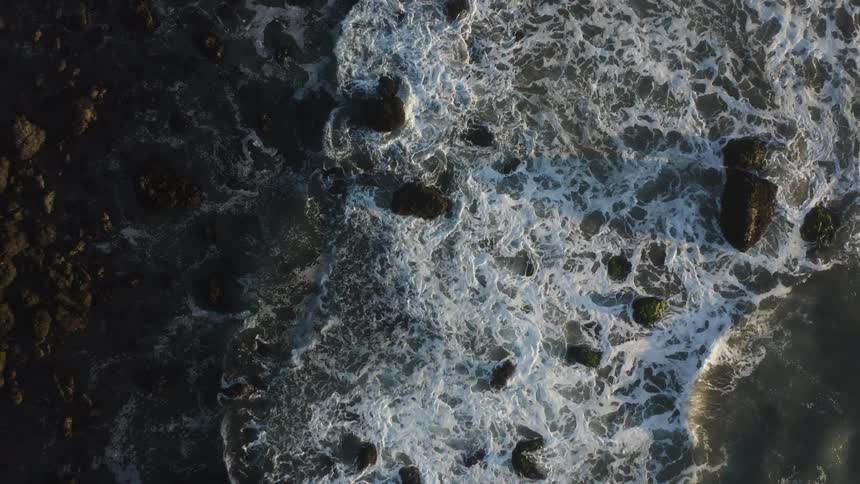 An aerial view of the ocean with waves breaking at the shoreline