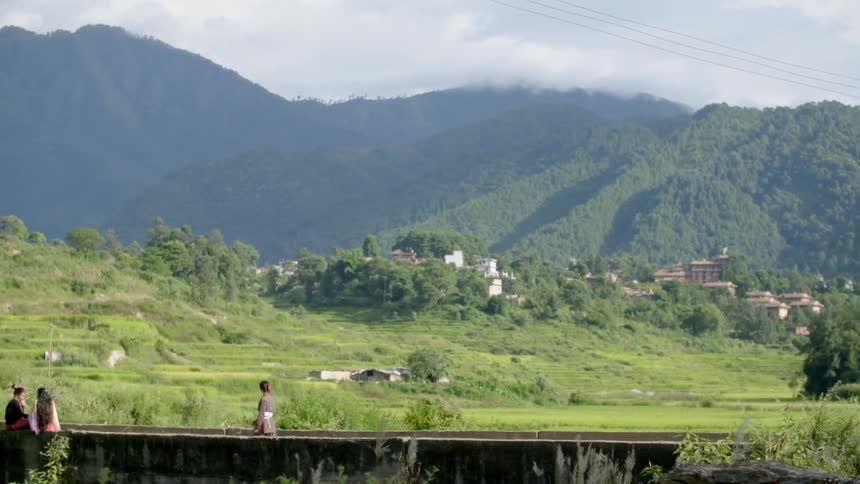 People are walking and sitting near a hilly area covered with grass