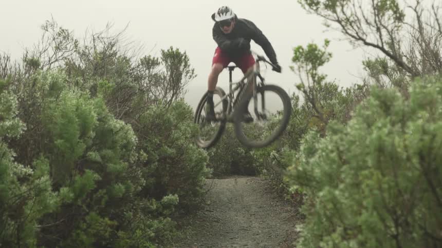 Person wearing helmet rides bicycle along trail jumping around curve