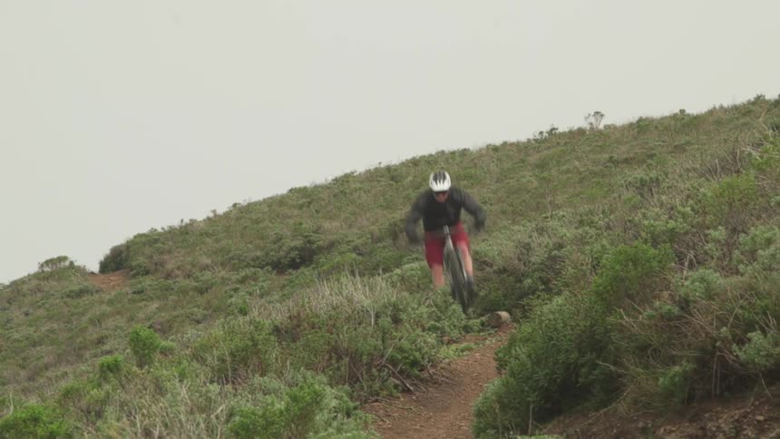 Cyclist wearing helmet rides mountain bike down rough hillside trail