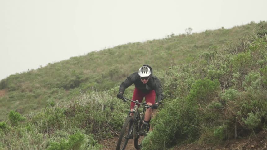 Cyclist wearing helmet and dark glasses rides a mountain bike down a trail on a hill