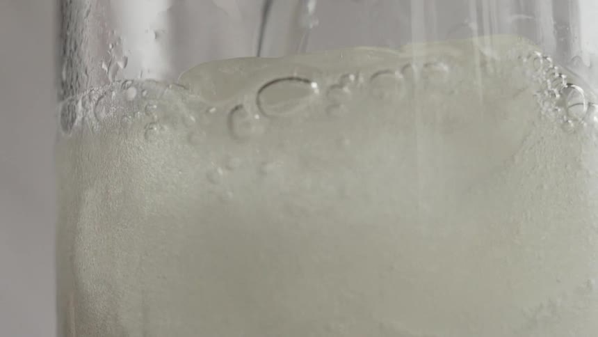A clear liquid beverage is poured in a glass pitcher of ice