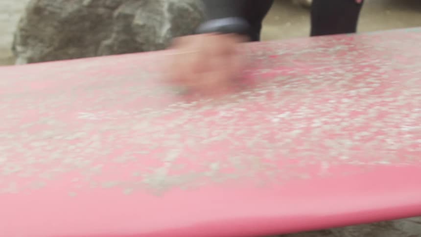 Barefoot woman wipes down and smooths out a surfboard