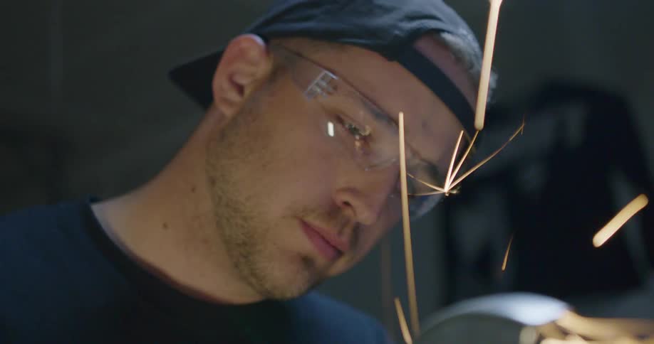 Man wearing protective glasses cuts metal on a vice with a power tool
