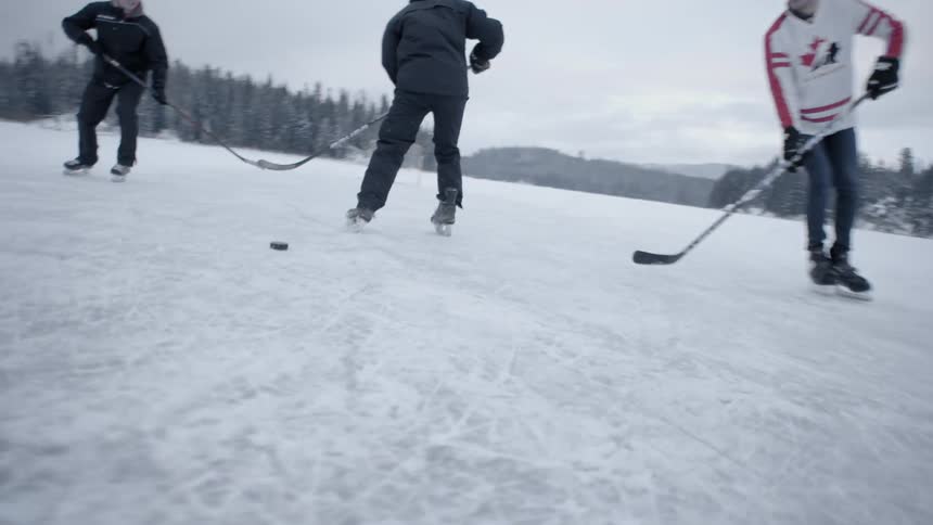 Three men play hockey on a frozen lake on a frigid winter day