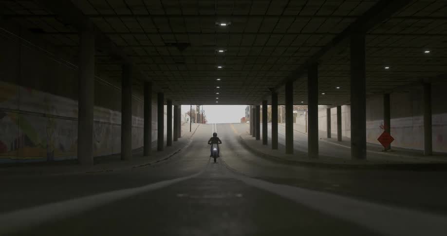 A person on a motorcycle drives under a bridge
