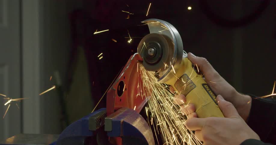 A person cutting a piece of metal on a vice with a power tool