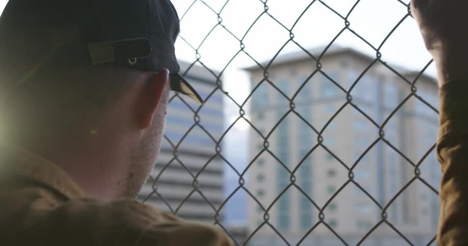 A man looks at skyscrapers through a chain link fence