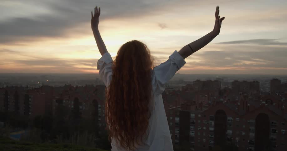 A teenage girl standing above a city skyline stretches her arms in to the air