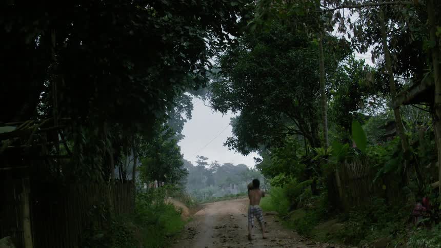 A boy is dribbling a basketball down a dirty trail
