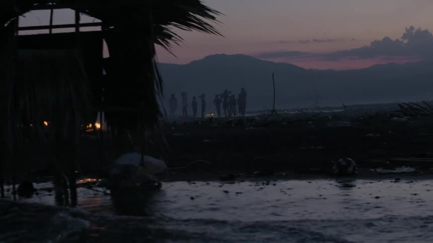 People gathered on a beach as bonfires burn during sun set