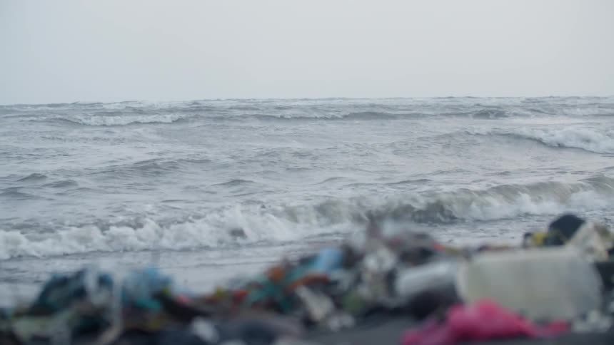 A shore has waves crashing and debris all over