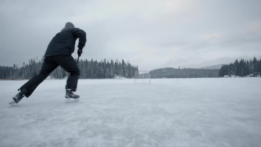 A man is pushing a hockey puck forward then drives it into a net