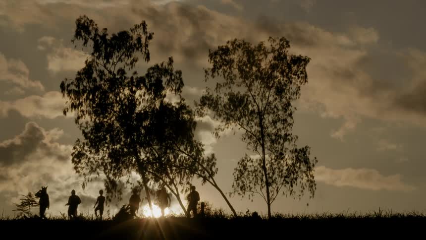 Armed men walk through a rural area at sunset