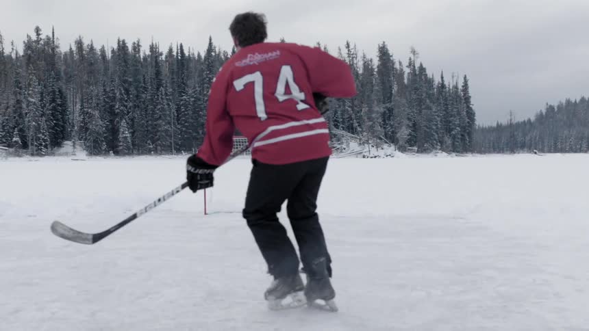 A hockey player shoots a puck at the net on a frozen lake