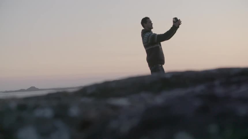A man is taking a photograph near the water at sunset