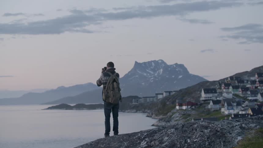 A man stands near a lake at dawn taking pictures