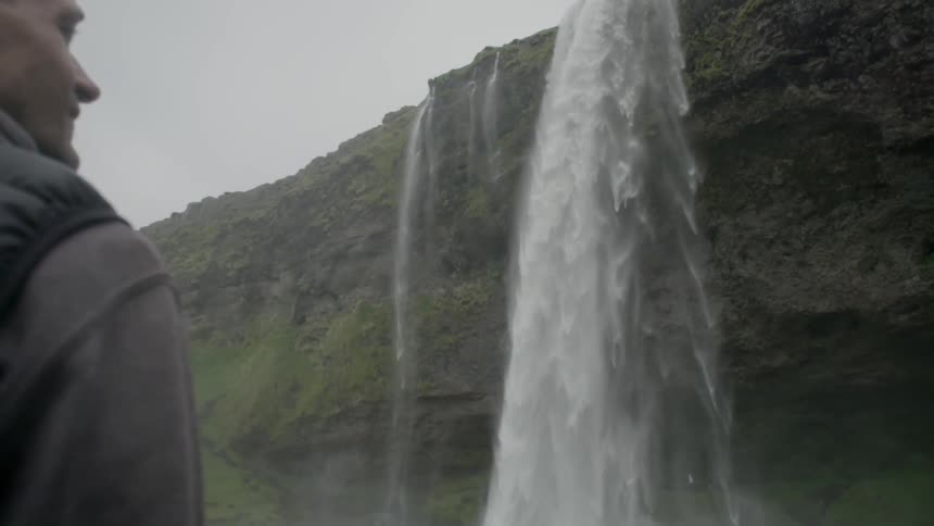 Man looking at a tall waterfall and smiling