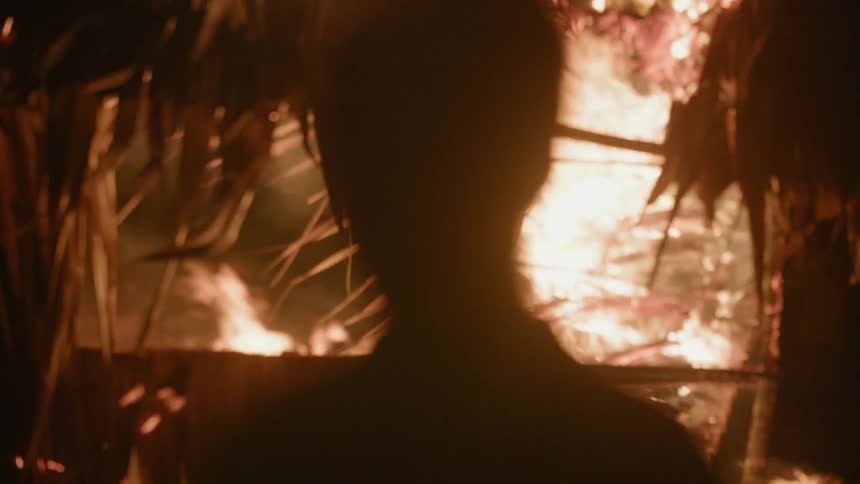 Person standing and looking towards a large blazing fire