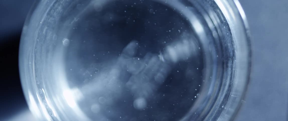 Clear glass with a liquid lightly shaking inside of it on a table