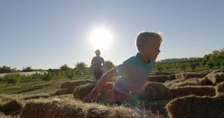 A young boy runs through bales of hay as his father and brother stand nearby