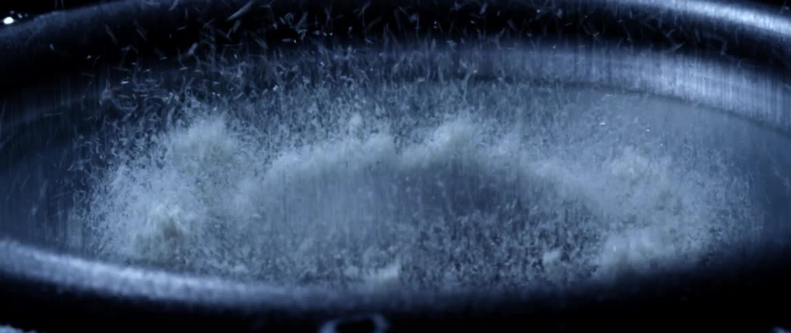 White particle bounces up and down as dark gray bowl trembles