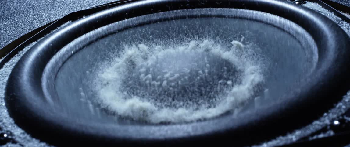 White dust jumping up and down over the vibrating surface of a speaker