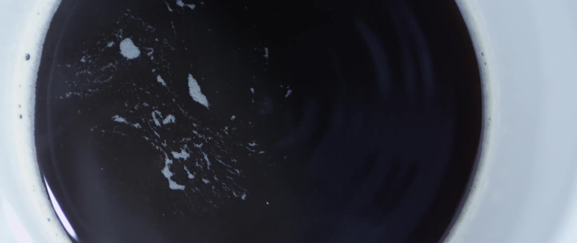 Black liquid is spinning inside a white container