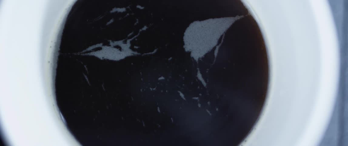 A white cup with brown coffee inside it smoking